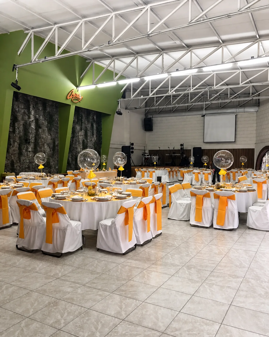 Interior del salón con mesas naranjas y blancas junto al escenario